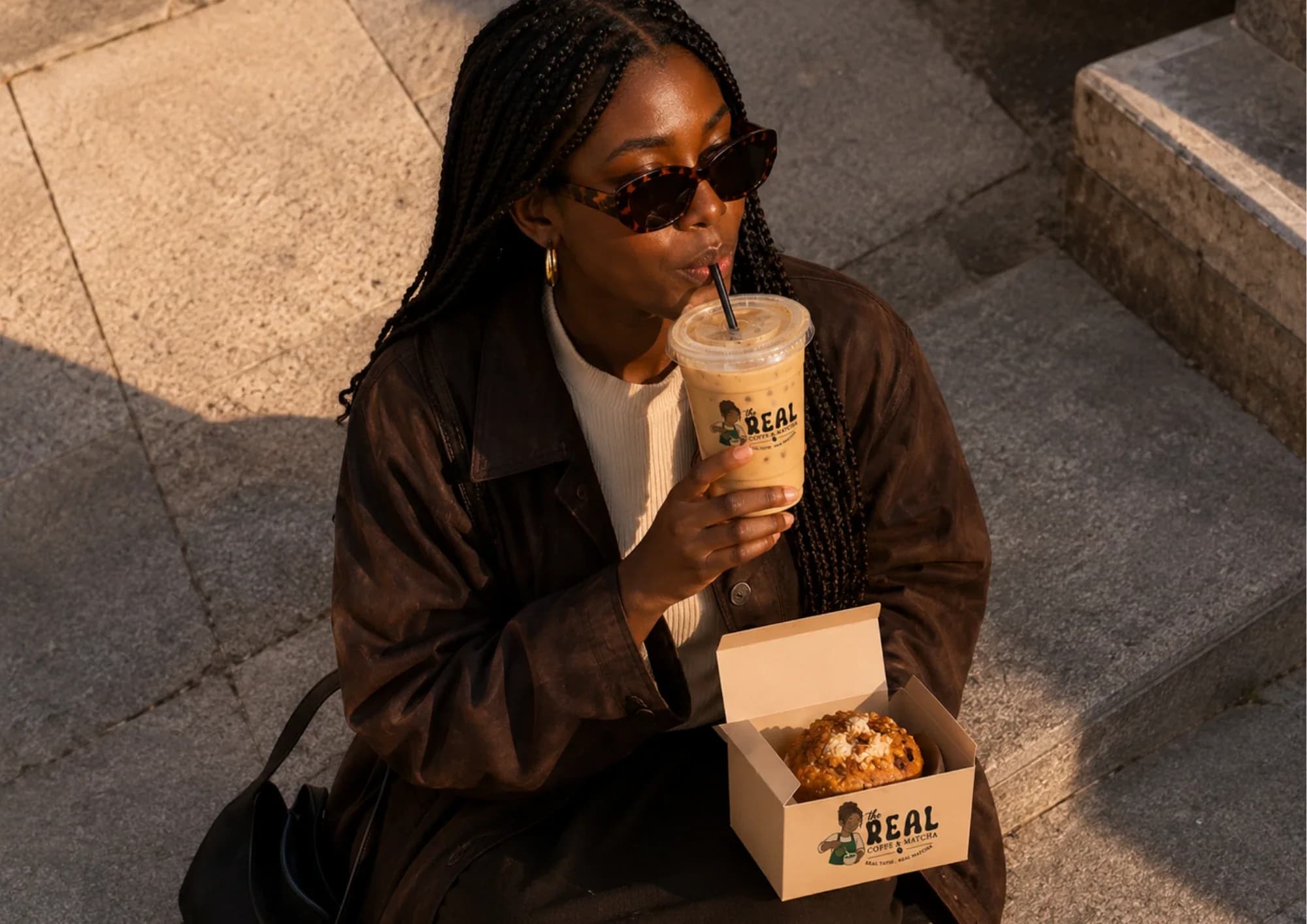 Cliente assise sur des marches, un latte glacé The Real à la main